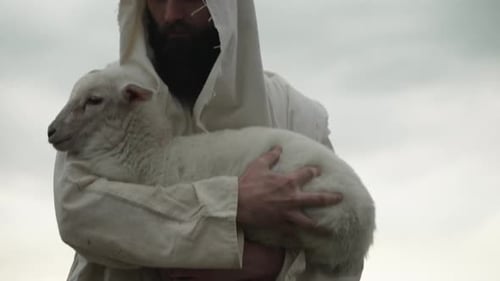Man in Robe Holds Lamb Gently Outdoors