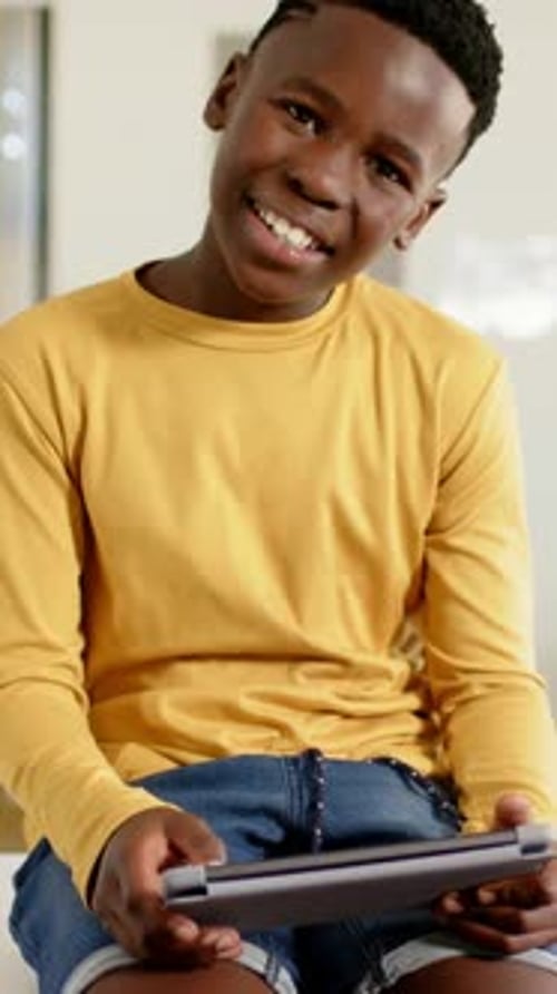 Vertical video: Tapping youth on stool at tablet, glancing up and laughing in class, yellow shirt
