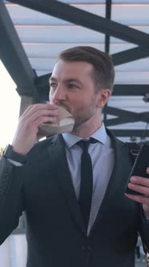 Young Man in Suit Eating Burger Outdoors