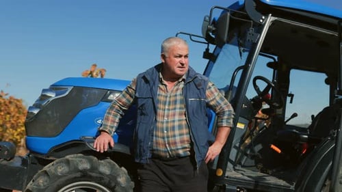 Seasoned Farmer Proudly Poses Beside Tractor in Rural Field