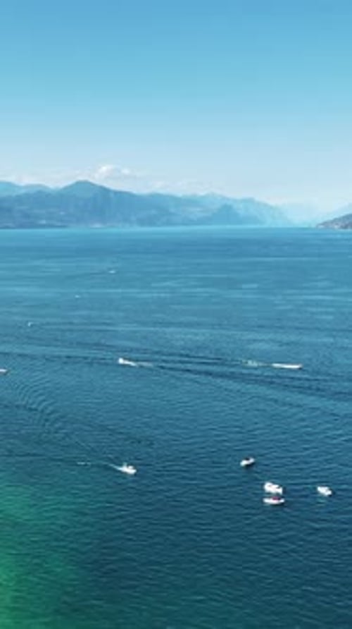 Aerial drone view the turquoise waters of Lake Garda with a small island and boats moving across the