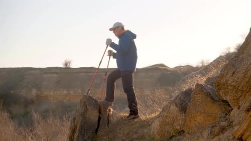 Tourist-Traveller Stands With Hiking Poles On A Rock And Looks Down
