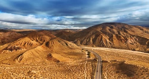 Dry desert with no greenery. Drone rising above the highway opening the view on bare mountains.
