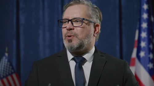 Man Giving a Speech in Front of Flags