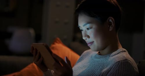 4k video footage of a young woman using a digital tablet on the sofa during the night at home
