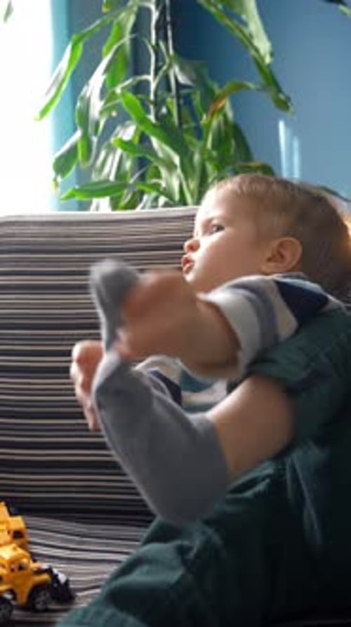 Vertical of Toddler Putting on Sock Cozy Living Room