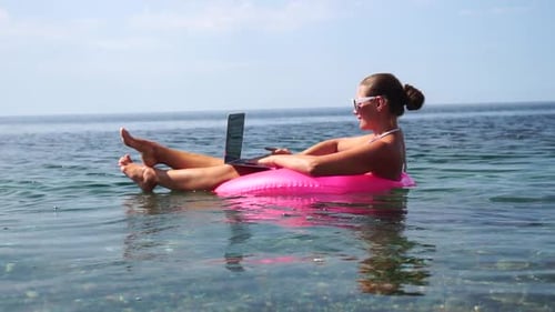 Woman Freelancer Works on Laptop Swimming in Sea on Pink Inflatable Ring Happy Tourist in Sunglasses