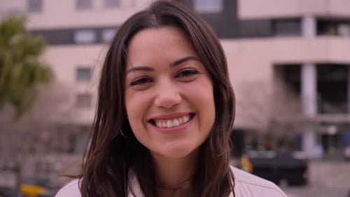Close Up Smiling Caucasian Woman Looks Flirtatiously at Camera Outdoors Background Urban Buildings