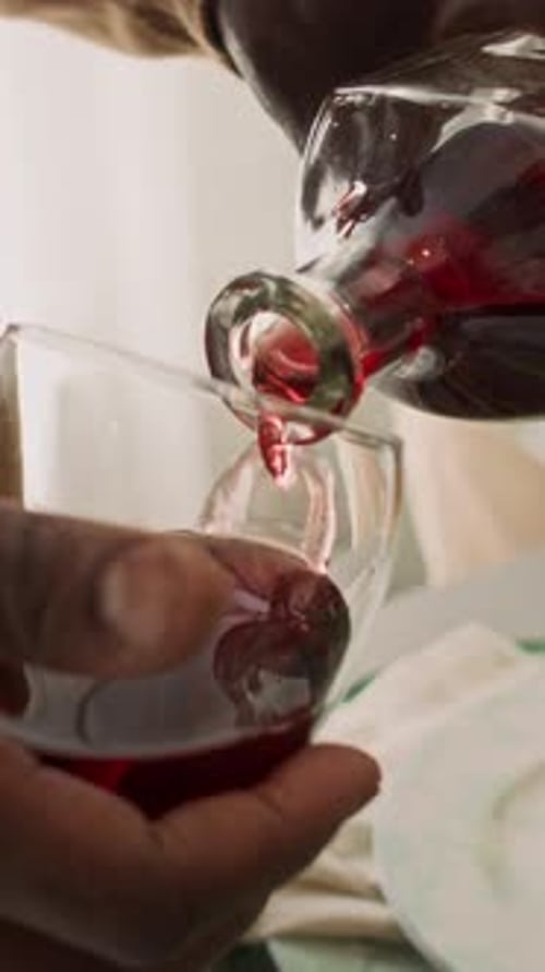 Hände eines anonymen schwarzen Mannes, der hausgemachten Wein in ein Glas gießt