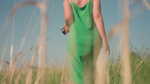 Woman in Green Dress Walking Through Sunlit Meadow with Calm Confidence