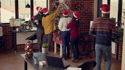 Colleagues Decorating Office Christmas Tree in Santa Hats