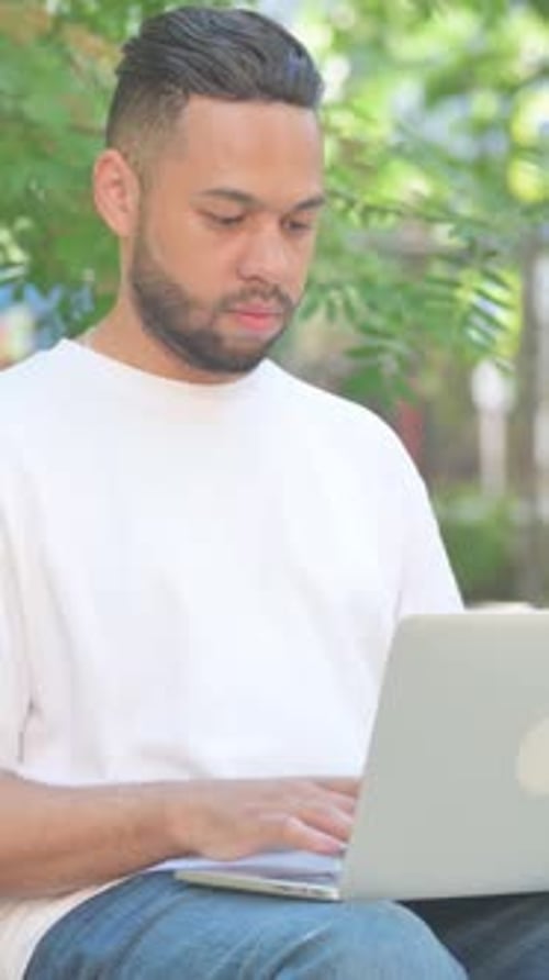 Vertikales Video, im Freien sitzender Mann mittleren Alters, der die Bank verlässt, nachdem er den Laptop geschlossen hat