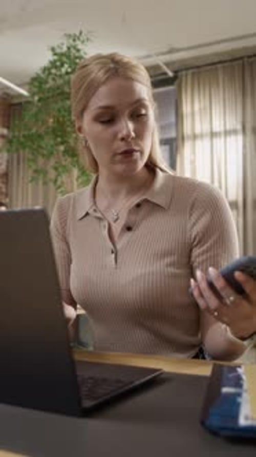 Vertical of Female Office Worker Using Laptop While Checking Smartphone
