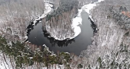 Aerial view of snowy forest and frozen river in winter.