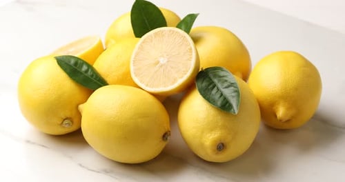 Fresh lemons with green leaves on white marble board, closeup