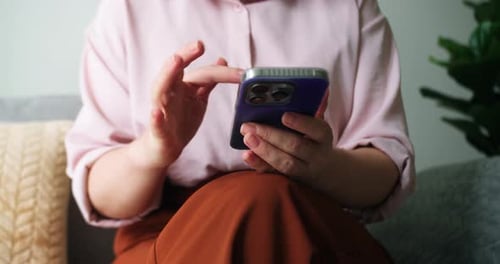 A Woman is Typing on a Mobile Phone Screen and Chatting While Sitting on the Sofa The Girl Uses the