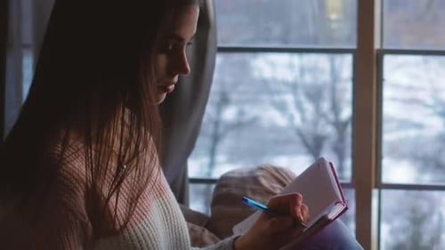 Woman Writing in Notebook by Window