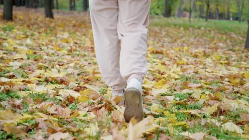 Close Up Feet in White Boots Walk on the Autumn Foliage with Golden Leaves