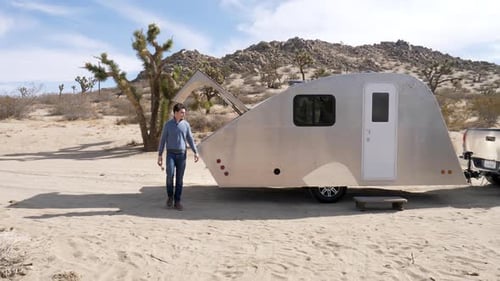 Slow motion shot of a handsome man in the desert on a camping trip in a metal teardrop travel traile