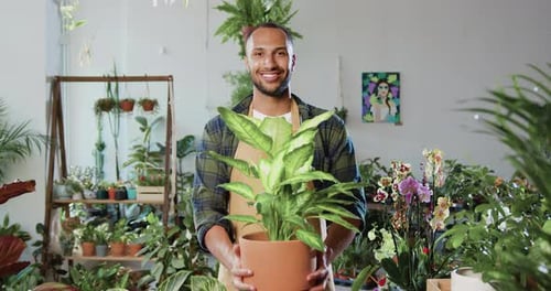 Portrait of good-looking contented botanical gardener worker in uniform standing in flower store and