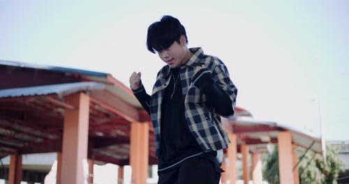 A hip-hop young man enjoys freestyle dancing in an outdoor pavilion.