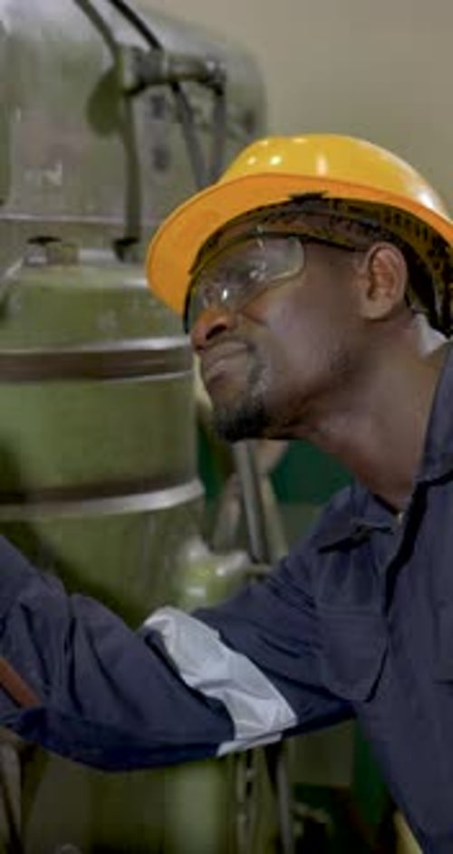 African male technician leans close to milling machine body, inspecting surface condition and