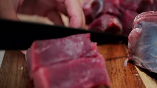 Close up of a woman cutting up raw beef on a wooden cutting board