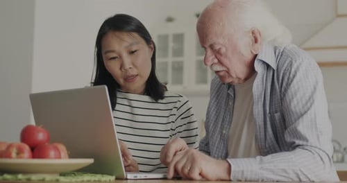 Woman Helping Senior Man with Laptop in Kitchen