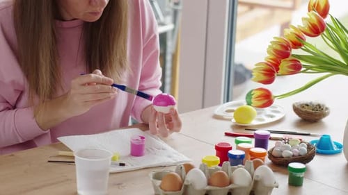 Frau malt Ostereier zu Hause für die Frühlingsferien