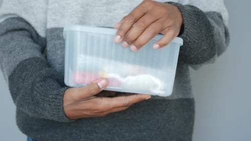 Mains tenant une boîte de rangement transparente avec divers articles à l'intérieur