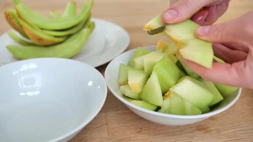 Melonenscheiben in Tellern auf einem Holztisch. Ansicht von oben. Mit den Händen Melonenscheiben schneiden