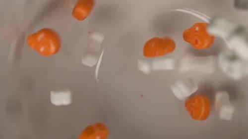 Close up of orange skulls and bones shaped candy slowly falling on a plate.