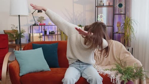 Une femme joyeuse et positive à la mode qui danse et bouge au rythme en faisant un geste de dub dance dans une maison moderne
