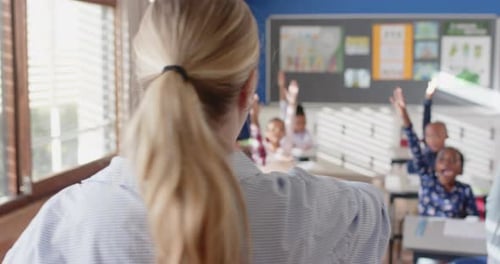 In school, female teacher calling on students raising hands in classroom discussion
