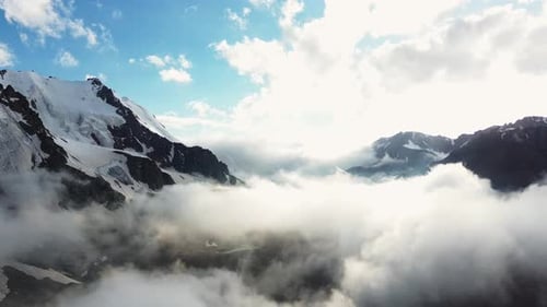 Aerial view of high mountains in clouds, backward camera move.