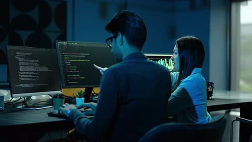 Two professional software engineers collaborating on an IT project late at night in modern workspace