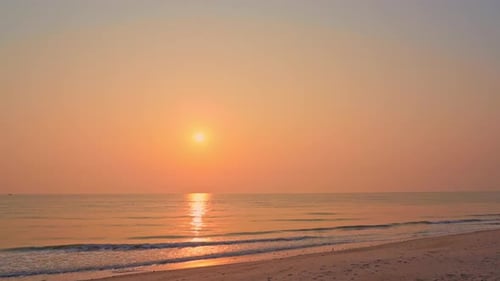 Amazing golden seaside sunset waves slowly rolling towards the sandy beach in Bali, camera pans left