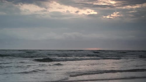 Low shot close to waves crashing to the shore as the sun is trying to peep out of the clouds on an o