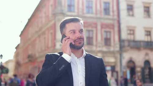 Close Up Portrait of Cheerful Caucasian Male Professional Standing in City and Talking on Smartphone