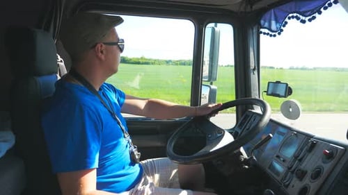 Profil eines Fahrers mit Sonnenbrille, der hinter dem Lenkrad seines Trucks sitzt und auf dem Land fährt