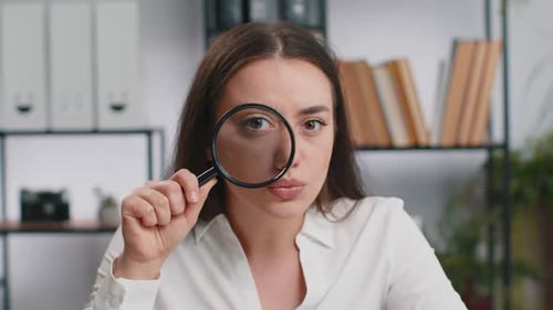 Geschäftsfrau, die Lupe in der Nähe des Gesichts hält, schaut mit großer gezoomter Augensuche und Analyse