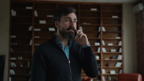 Man Speaking on Phone in Front of Bookshelf