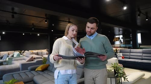 Young Couple Chooses Sofa on the Catalog in Luxury Furniture Shop