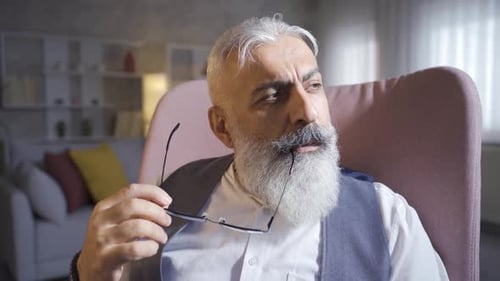 The old man is thinking, playing with his beard and glasses.