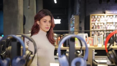 Young Happy Woman Chooses Headphones in a Store