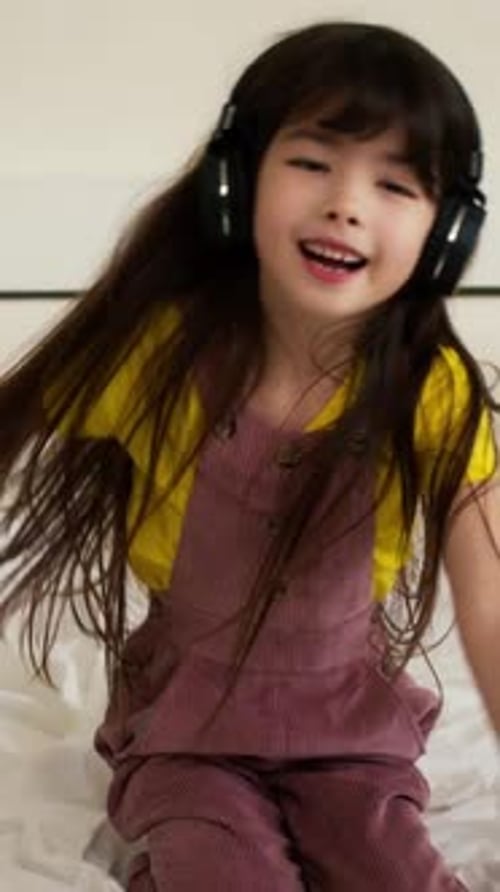 Happy Girl Listens to Music on Bed