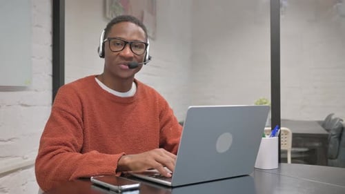 Young Adult Using Laptop and Headset in Office