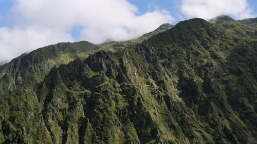 Aerial approach to a beautiful mountain in summer, the trees are green, the clouds pass in a blue sk