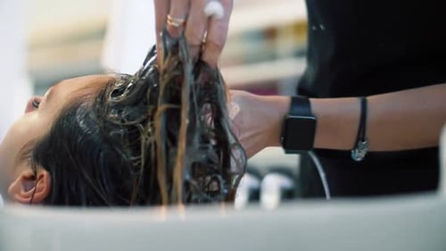Der Friseursalon wäscht die Haare des Kunden mit dem Kopf über dem Waschbecken. Frau lässt sich in s die Haare waschen
