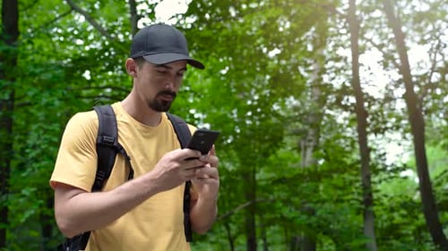 Face Man with Backpack in Forest Uses Phone to Touch the Screen Looking for Connection Signal